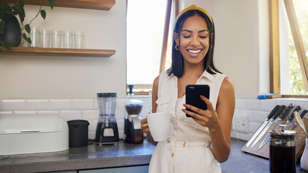 woman in kitchen drinking coffee smiling on summers day looking at phone